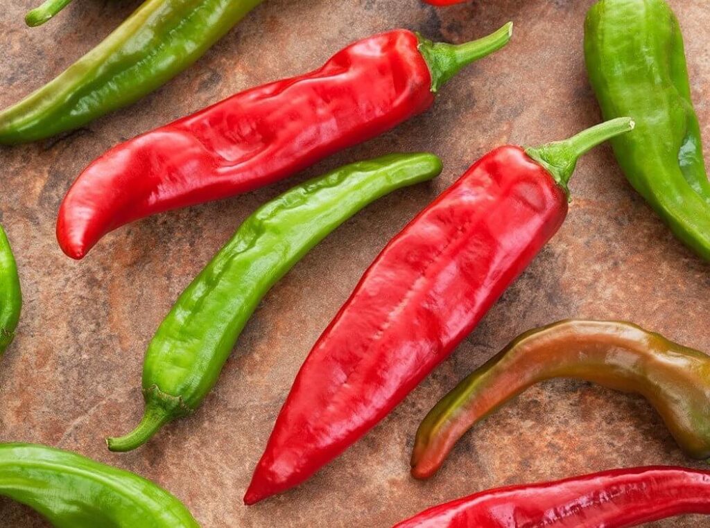 Red and green chile peppers arranged on a brown surface.