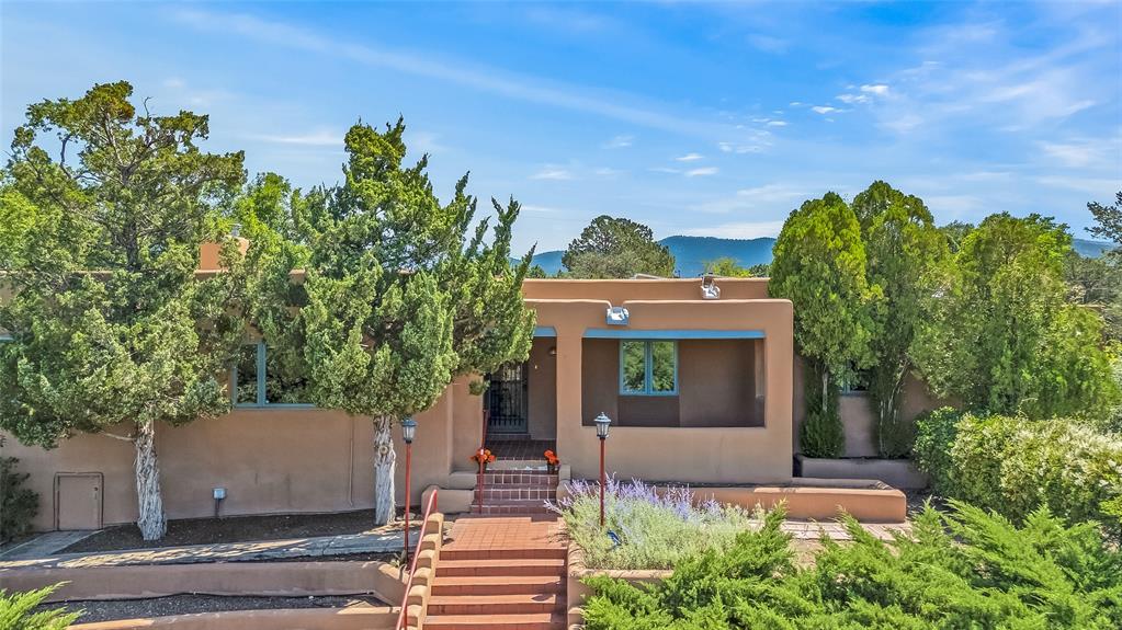 Single-story stucco Santa Fe home with front steps, mature trees, and landscaped shrubs.