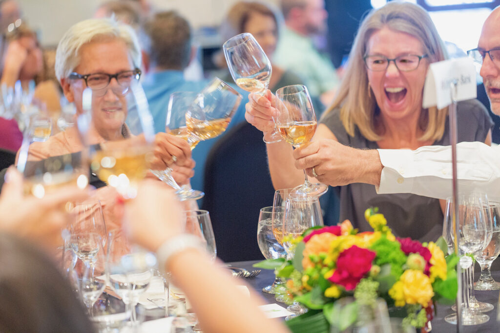 Guests toast with glasses of white wine at a lively Santa Fe Wine & Chile Fiesta gathering.
